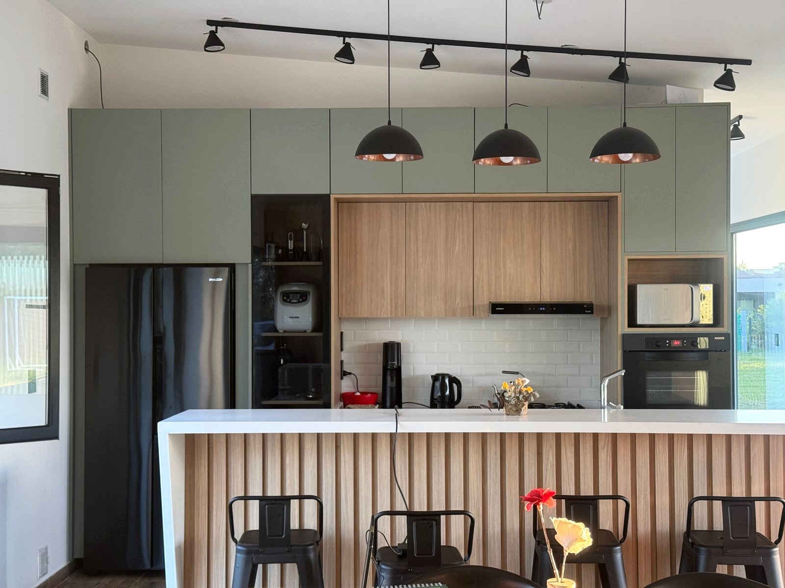 Cocina con frentes verdes y barra revestida en madera